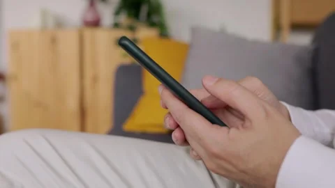 Close up view of a man using mobile smart phone sitting on sofa at home Stock Footage 261389551