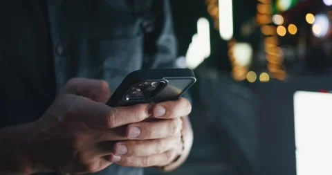 Close-up view of a man's hand using a smartphone among the glowing lights of Stock Footage 251022170