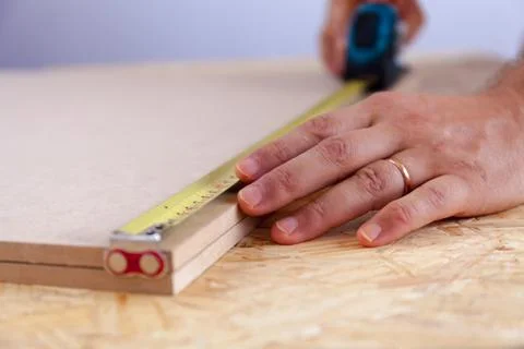 Close up view of a man's hands measuring a piece of wood with a tape. Handyman Foto stock