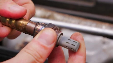Close up view of a mechanic inspecting an oxygen sensor, turning the component Stock Footage 283682309