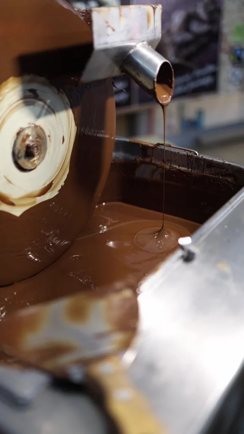 A close-up view of melted chocolate flowing smoothly from a machine in a chocola Stock Footage 289634689