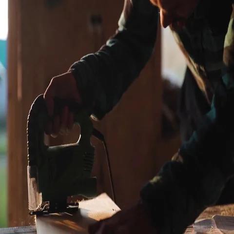 Close-up view of men working with electric jigsaw and wooden plank. sun flare on Stock Footage 69540181