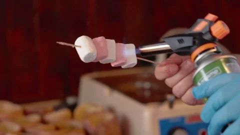 Close up view of men's gloved hands making a caramel crust on a marshmallow with Stock Footage 244635341