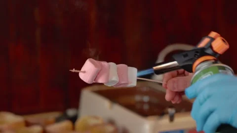 Close up view of men's gloved hands making a caramel crust on a marshmallow with Stock Footage 244828727