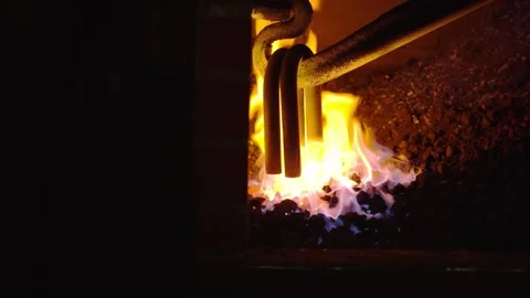Close view of metal chain links heating in fire inside a blacksmith forge with Stock Footage 328993219