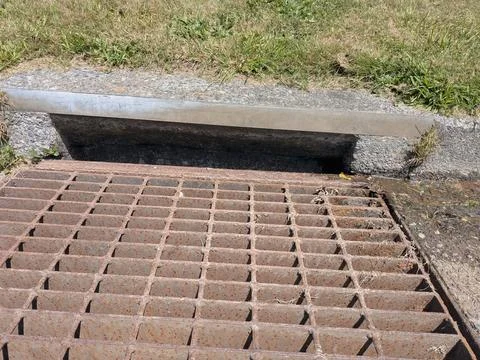 A close-up view of a metal storm drain grate set into concrete Stock Photos