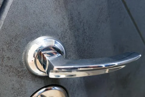 Close-up view of a modern door handle on a textured gray door surface showing Photos
