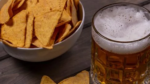 Close-up view of a mug of cold frothy beer with nachos corn chips on a wooden Stock Photos