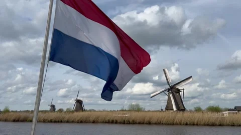 Close-up View to the Netherlands flag and wooden windmills at sunset Stock Footage 318998813