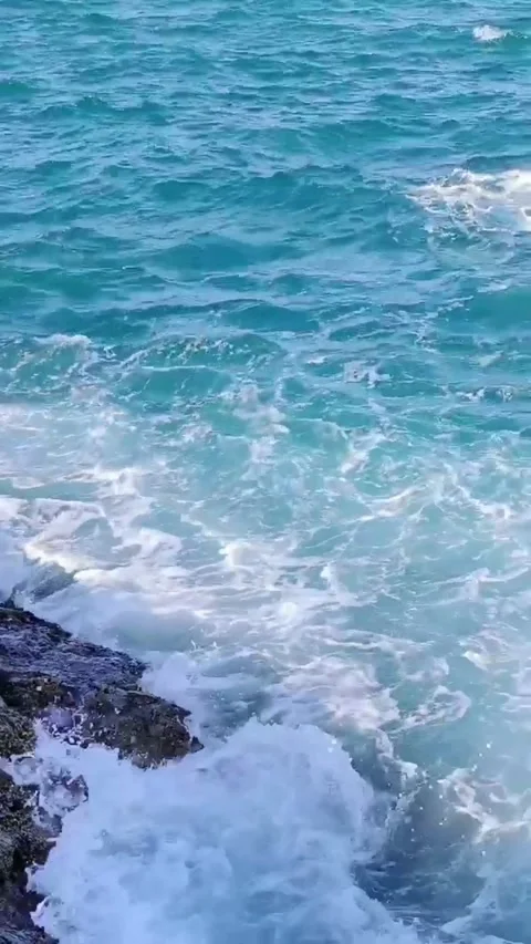 Close-up view of ocean waves crashing on rocky coastline, clear blue water and Vidéo 333605140