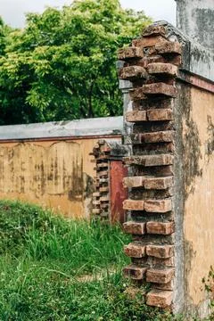 Close view of an old brick pillar projecting from a weathered wall with greenery Stock Photos