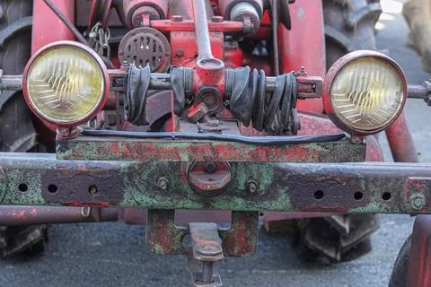 A close-up view of an old red tractor showcases its weathered headlights and  Stock Photos