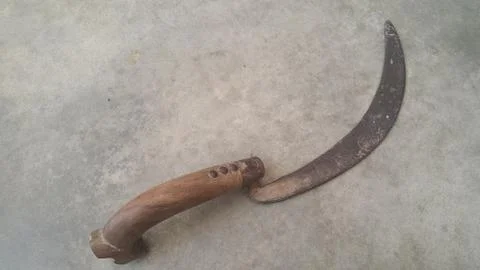 Close-up view of an old sickle (reaping-hook) on the concrete surface Stock Photos