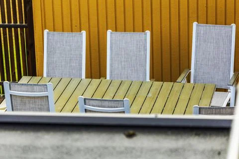 Close-up view of outdoor dining table with chairs beside wooden house wall. Stock Photos