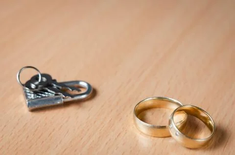 Close up view of a padlock with key  next to two wedding rings representing a Stock Photos