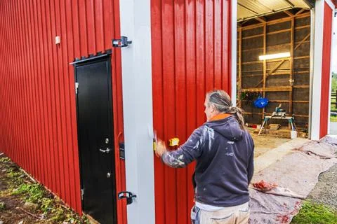 Close up view of painter applying red paint to wooden barn exterior beside Stock Photos
