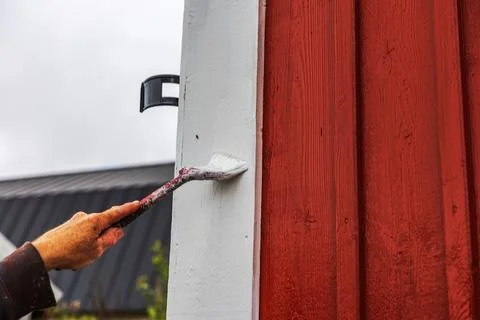 Close-up view of painter applying white paint to wooden trim beside Stock Photos