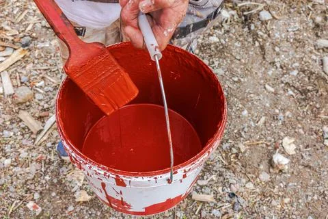 Close-up view of painter holding brush over bucket of red exterior facade paint. Stock Photos