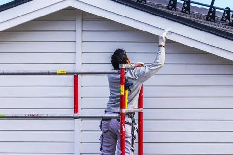 Close-up view of painter working on scaffold while painting wooden house facade Stock Photos