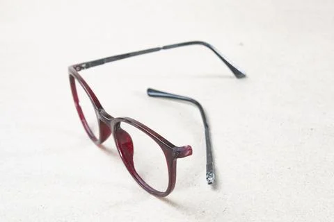 A close-up view of a pair of broken eyeglasses resting on a light-colored s.. 写真素材