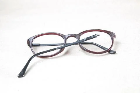A close-up view of a pair of broken eyeglasses resting on a light-colored s.. Фото