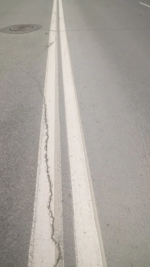 Close-up View of Parallel Road Lines on Asphalt Surface with Manhole Cover in Stock Footage 312674494