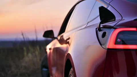 Close view of a parked red electric car opening charging port at sunset Stock Footage 235283137