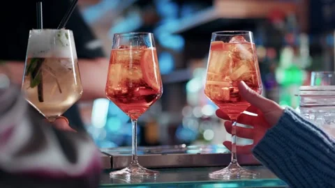 Close view of people lifting orange cocktails and white wine glasses from a bar 動画素材 348799570