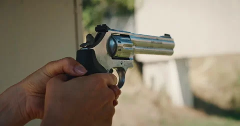 Close-up view of a person aiming and firing a silver revolver at shooting range Stock Footage 313730619