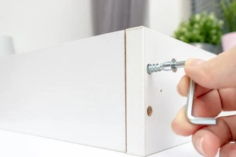 Close up view of a person assembling new white drawer using a screwdriver, ti Stock Photos