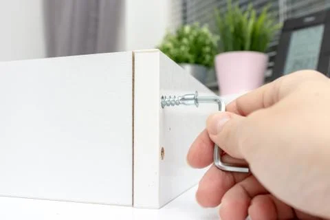 Close up view of a person assembling new white drawer using a screwdriver, ti Stock Photos