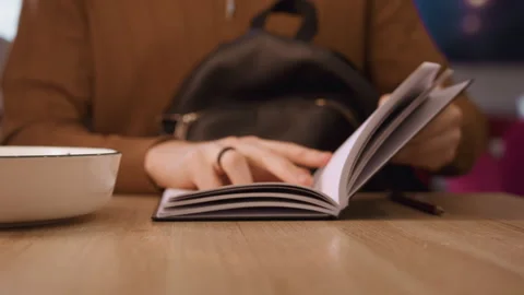 Close up view as person flips through notebook pages on wooden table with soft Stock Footage 344868728