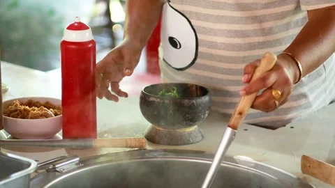 A close-up view of person preparing street food, pouring liquid from a ladl.. Stockbeeldmateriaal 333696226