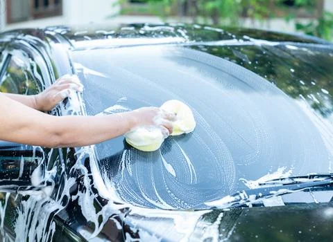 A close-up view of a person's hands actively washing the windshield and hoo.. Foto stock