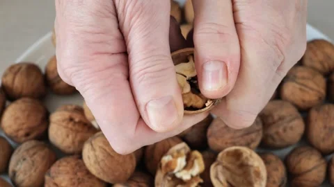 Close up view of a person's hands cracking open a walnut over a bowl. Video stock 327114875