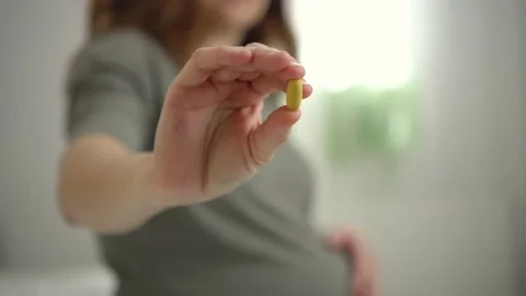 Close-up view of pill in hand. In the background is pregnant woman. Taking Stock Footage 171373461