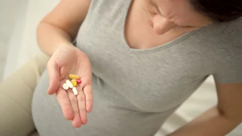 Close-up view of pill in hand. In the background is pregnant woman. Taking Stock-Footage 171685538