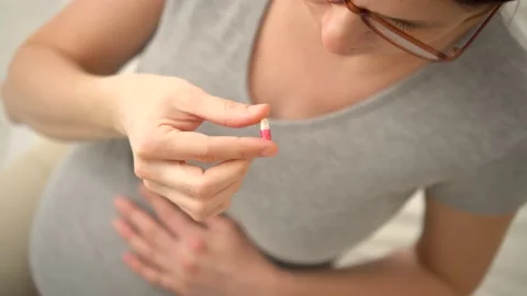 Close-up view of pill in hand. In the background is pregnant woman. Taking Video stock 171772644