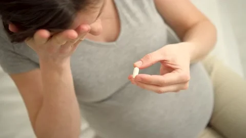 Close-up view of pill in hand. In the background is pregnant woman. Taking Video stock 185047796