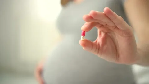 Close-up view of pills in hand. In background is pregnant woman. Taking vitamins Video stock 171685372