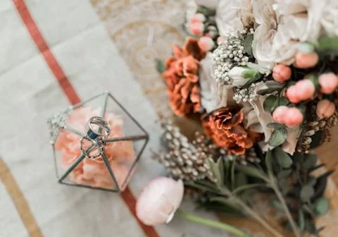 Close up view of pink flowers, wedding rings in rustic box on table Stock Photos