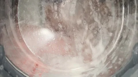 Close up view of pink laundry tumbling inside washing machine drum through .. Stock Footage 339386855