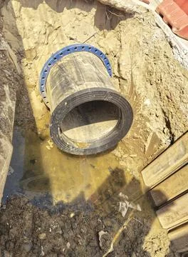 Close-up view of pipe with a blue fitting and water in a trench Stock Photos
