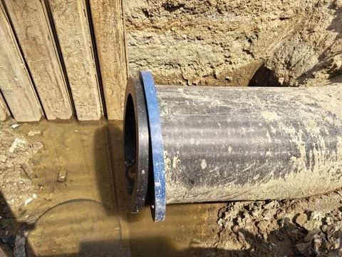 Close-up view of pipe with a blue fitting and water in a trench Stock Photos
