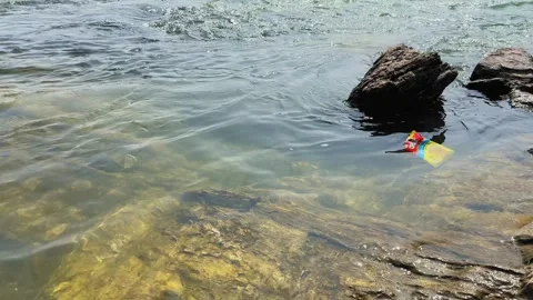 Close view of a plastic packet floating in clear flowing river water near Видео 331043274