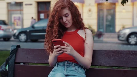 Close up view of positive redheaded curly student girl sitting on a bench in Stock Footage 115669872