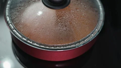 A close-up view of a pot lid with steam condensing on the glass. The pot sits on Stockbeeldmateriaal 337111893