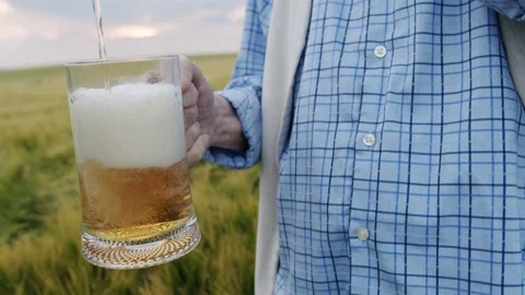 Close view of pouring beer with foam into a pint in male hand among barley field Vídeo Stock 141596838
