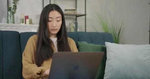 Close up view pretty concentrate young asian woman sitting on couch using laptop Vídeos de archivo 194170292