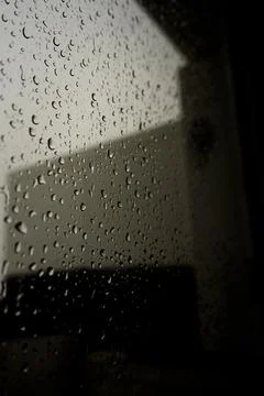 A close-up view of raindrops on a windowpane, with a dark background and a sl Stock Photos